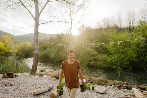 Photo of a young man carrying flower pots and working in his garden, planting different kinds of plants, and rebuilding his garden by the river.