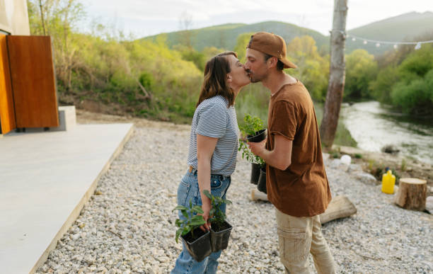 Photo of a young couple sharing their love and affection while working in their garden by the river, planting different kinds of plants, and rebuilding their yard.
