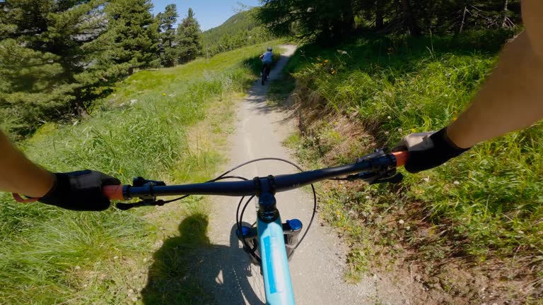 Mountain bikers ride along mountain trail in the morning. POV perspective view, biking along mountain slope.