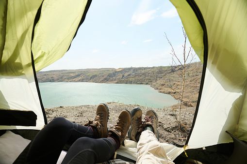 POV of two unrecognizable young women relaxing in camp tent on spring day enjoying beautiful view of quarry lake