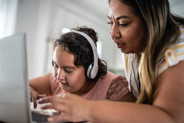 matka pomagająca dziewczynie z upośledzeniem psychoruchowym za pomocą laptopa uczącego się w domu - home schooling audio zdjęcia i obrazy z banku zdjęć