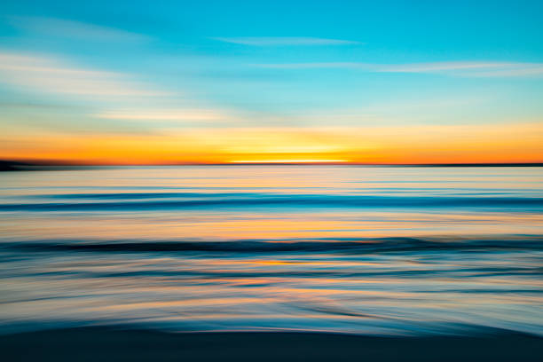 istock Calm coastal sunset beach scene, motion blurred with ocean water reflecting a bright dramatic sunset 1405305193