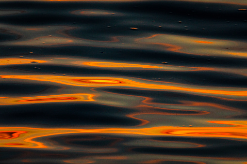 Close up of ocean water surface reflecting a bright orange sunset, California, USA.