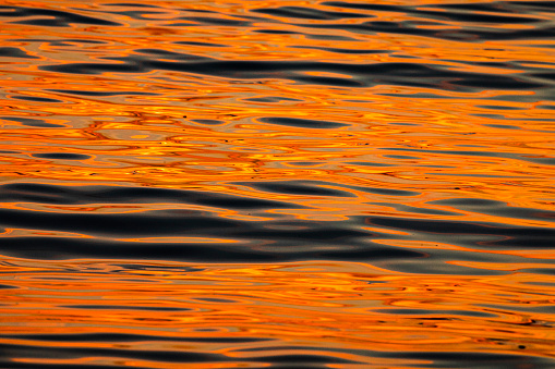 Close up of ocean water surface reflecting a bright orange sunset, California, USA.