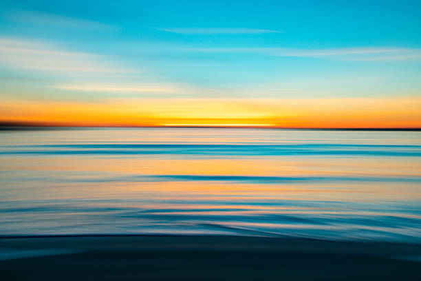 Calm coastal sunset beach scene, motion blurred with ocean water reflecting a bright dramatic sunset, California, USA.