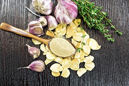 Ground garlic in a spoon, dried and fresh garlic, bunch of thyme on wooden board background from above