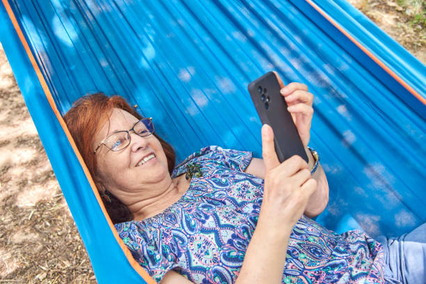 istock Hispanic mature woman smiling using her smart phone lying in a blue hammock. 1405327778