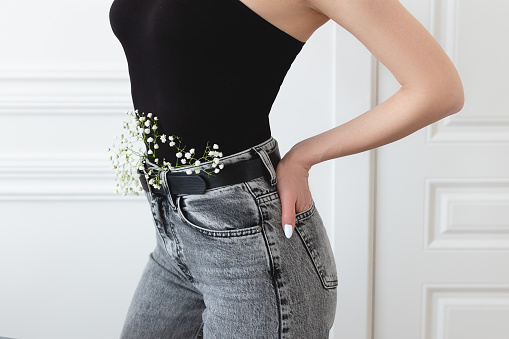 Silhouette of a slender girl in dark clothes on a white background with flowers in her belt.
