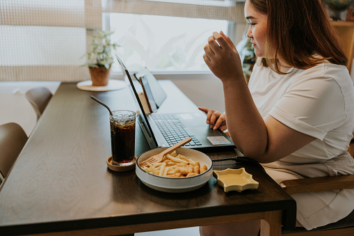 Plus-size woman working hard at home and enjoy eating fast food that she ordering from delivery application.