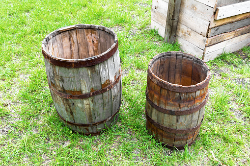 Old wooden barrels stand on the grass in the backyard in the village. Texture of weathered wood