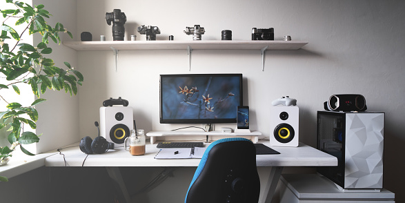 Front view comfortable home office workplace of photographer with computer, camera lens different types. White minimalistic interior for working, business and entertainment digital online game playing