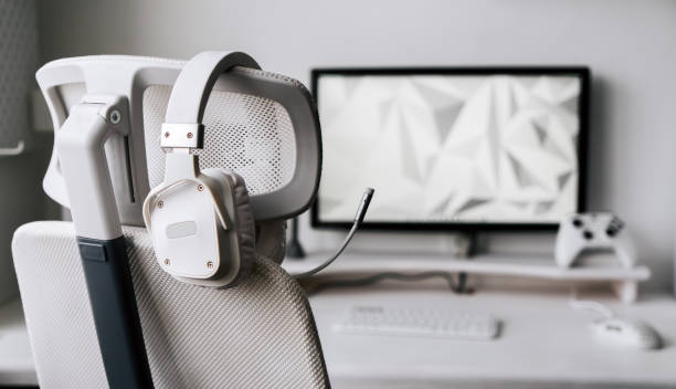 White large gaming headphones with a microphone hang on a white armchair. Close-up White large gaming headphones with a microphone hang on a white armchair. Close-up on the background of a light interior. gaming chair photos stock pictures, royalty-free photos & images