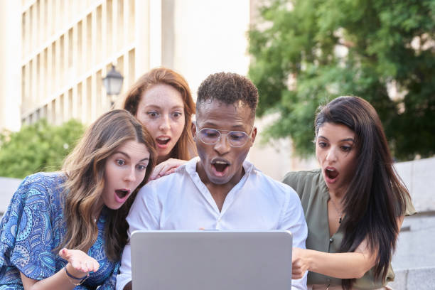 istock Group of multiracial people looking shocked at the laptop screen while using it outdoors in the street. 1405349026