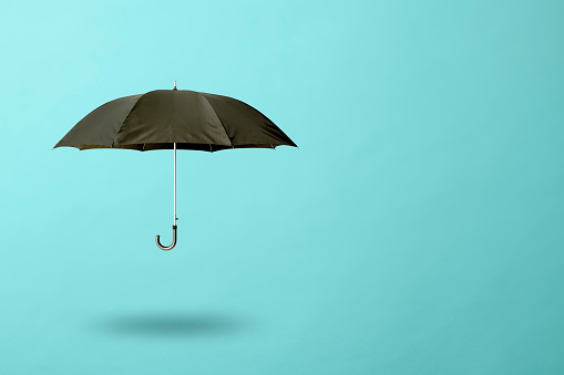 Black umbrella floating in mid-air against light blue background with copy space.