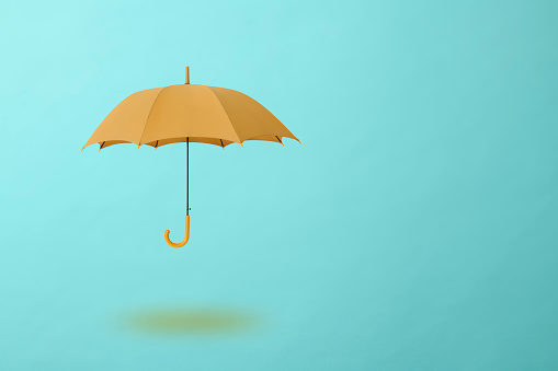Ocher umbrella floating in mid-air against light blue background with copy space.