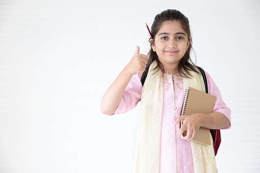 cute Indian girl holding notebook for learning and thumbs up pose, education concept