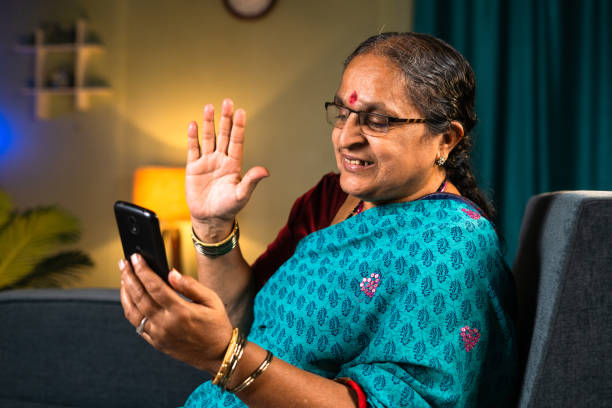 istock Old women making video calling on mobile phone while sitting on sofa at home - concepts of technology, relaxation and enjoyment. 1405363549