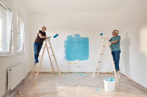 Happy senior couple communicating while painting their walls during home renovation process. Copy space.