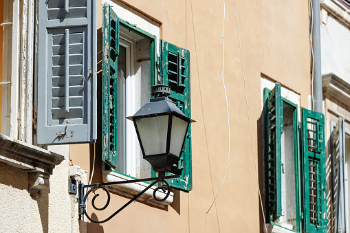 Windows with open wooden shutters and lantern attached to a building wall in Rovinj, pastel colored facade