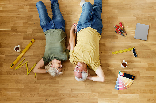 High angle view of happy mature couple talking while lying on the floor during a break from renovating their new apartment. Copy space.