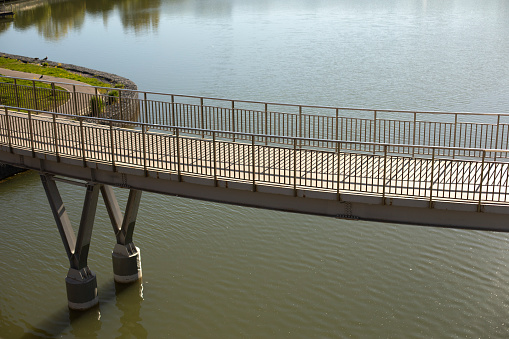Pedestrian bridge on water. Bridge with railings. Details of park in city. Embankment on lake.