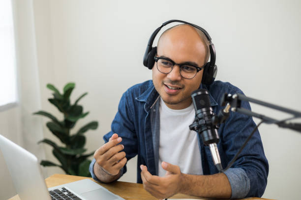 istock Content creator asia man host streaming his a podcast on laptop with headphones and condenser microphone interview guest conversation at home broadcast studio. Male blogger recording voice over radio 1405368821