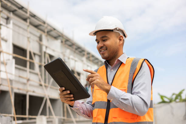 istock Confident asian engineer man Using tablet for checking and maintenance to inspection at modern home building construction. Architect working with white safety helmet in construction site 1405368823
