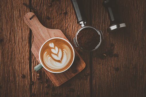 Latte art on hot latte coffee. Aroma coffee cup and coffee beans on wooden desk.