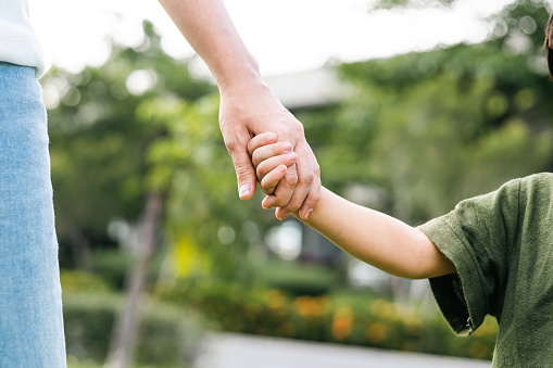 Moment happy family. Mom and boy a hold hands in park with sunlight. Smiles of children who are happy to spend time with their mothers on weekends. Parent happiness.