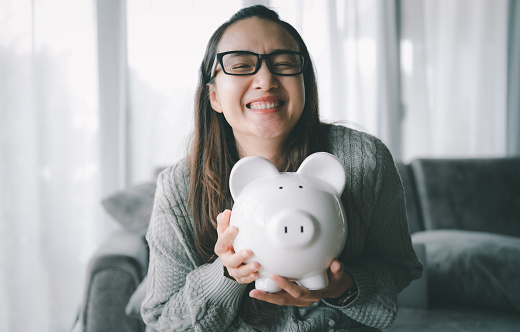 Happy smart Asian woman saving money in a piggybank. saving and money concept.