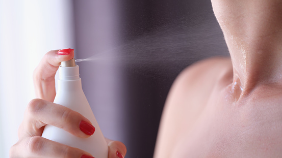 Woman with red manicure applying perfume on her neck closeup. Selection of women toilet water concept
