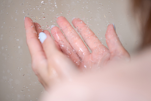 Close-up shot of female hands and water drops. Woman taking shower in the bathroom.