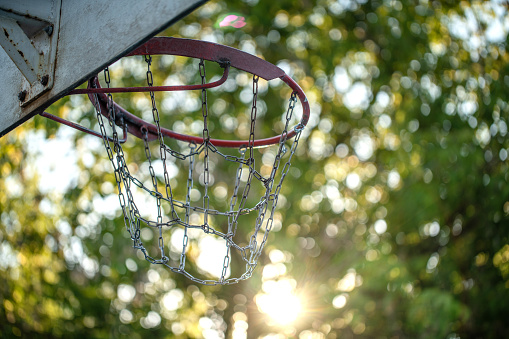 Basketball hoop with a metallic chain net at dawn, defocused trees on the background