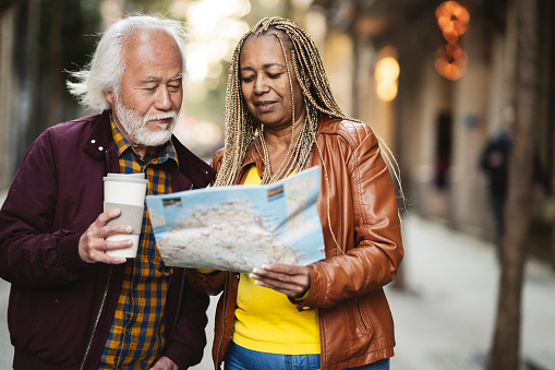 multiracial senior couple traveling in the city with a map, pretty seniors traveling retirees