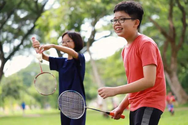 Photo of cheerful Asian boy and girl playing badminton in a park