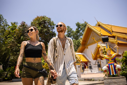 Caucasian couple holding hands, while visiting Thai temple, during their vacation