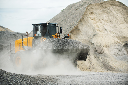 Sand loaders are shoveling rocks into dump trucks.\