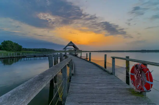 Swinging curved pier construction and shelter with thatched roof at lake Hemmelsdorf, Schleswig-Holstein, Germany. Winding wooden footbridge, bird platform and lifebelt on the lake Hemmelsdorf.