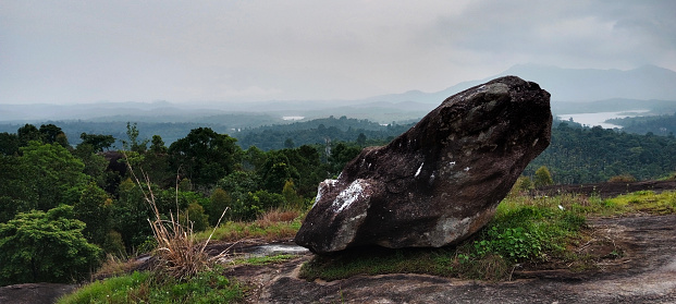 A big rock at the top of a mountain covered with forest