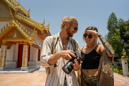 Caucasian couple looking at the photos on the camera they took while visiting Thai temple