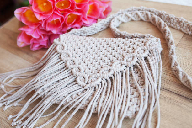 Handmade macrame cotton ross-body bag. Eco bag for women from cotton rope with bouquet of flowers in kraft paper. Scandinavian style bag.  Beige tones, sustainable fashion accessories. Close up image stock photo
