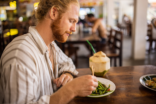 Side-view of Caucasian man eating Thai food with chopsticks