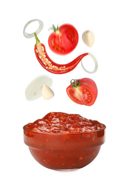 istock Different ingredients falling into glass bowl with delicious adjika sauce on white background 1405387824