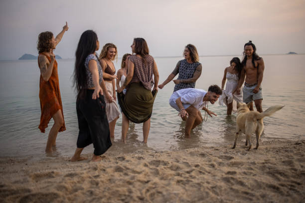 Urban multiracial female and male friends dancing on the beach during sunset while stray dog makes them a company