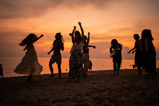 Group of multiracial female and male friends, enjoy the sunset on the beach, while dancing and playing guitar