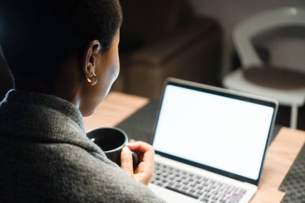 istock Young black woman, holding cup of coffee, looking at computer screen 1405389680