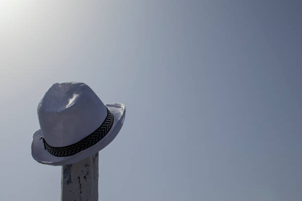 istock Close-up of a hat hanging on a pole against a blue sky. A white hat hanging from some old pole on the beach. A girl's hat hanging on a wooden pole from a fence. 1405391133