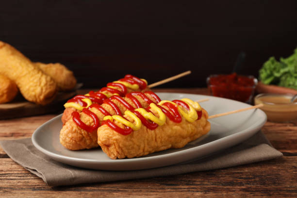 deliciosos perros de maíz con mostaza y ketchup sobre mesa de madera - corn dog fotografías e imágenes de stock