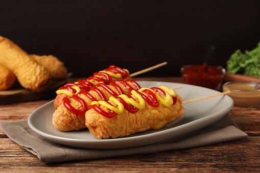 Delicious corn dogs with mustard and ketchup on wooden table