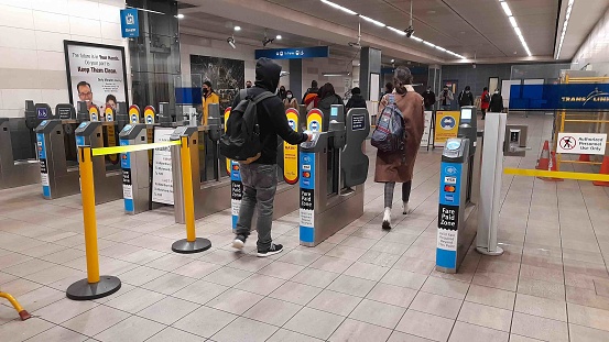 People Wearing Face Mask Due To Coronavirus, Checking In And Out With A Public Transportation Card At Access Gate Of Vancouver City Metro In British Columbia Canada